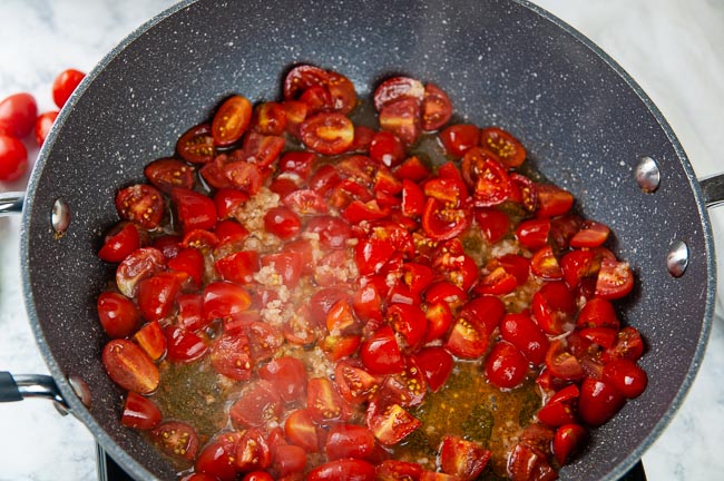 Halved cherry tomatoes sauteing in a skillet