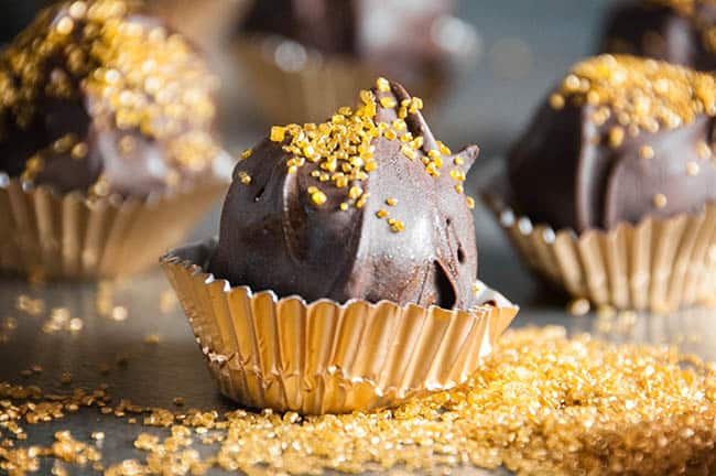 Chocolate dipped cookie dough candies with gold sprinkles and gold wrappers