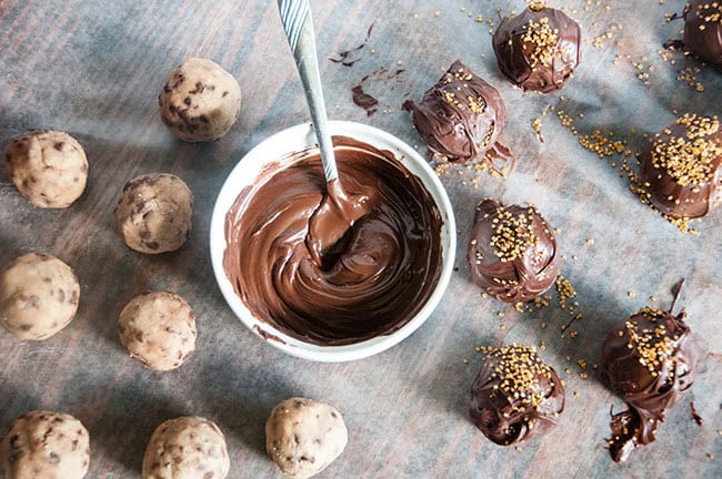 Cookie dough balls being dipped in chocolate and covered with sprinkles