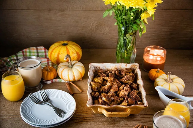 Pumpkin French Toast Casserole in a yellow baking dish with pumpkins and mums on the breakfast table