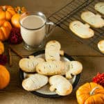 Pumpkin hand pies on a plate on a wood table with coffee, pumpkins, flowers, a candle, and cinnamon sticks