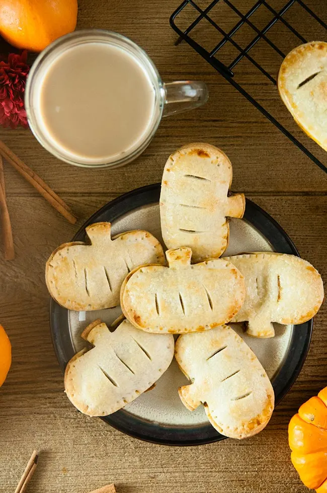 Pumpkin hand pies on a plate on a wood table with coffee, pumpkins, and cinnamon sticks