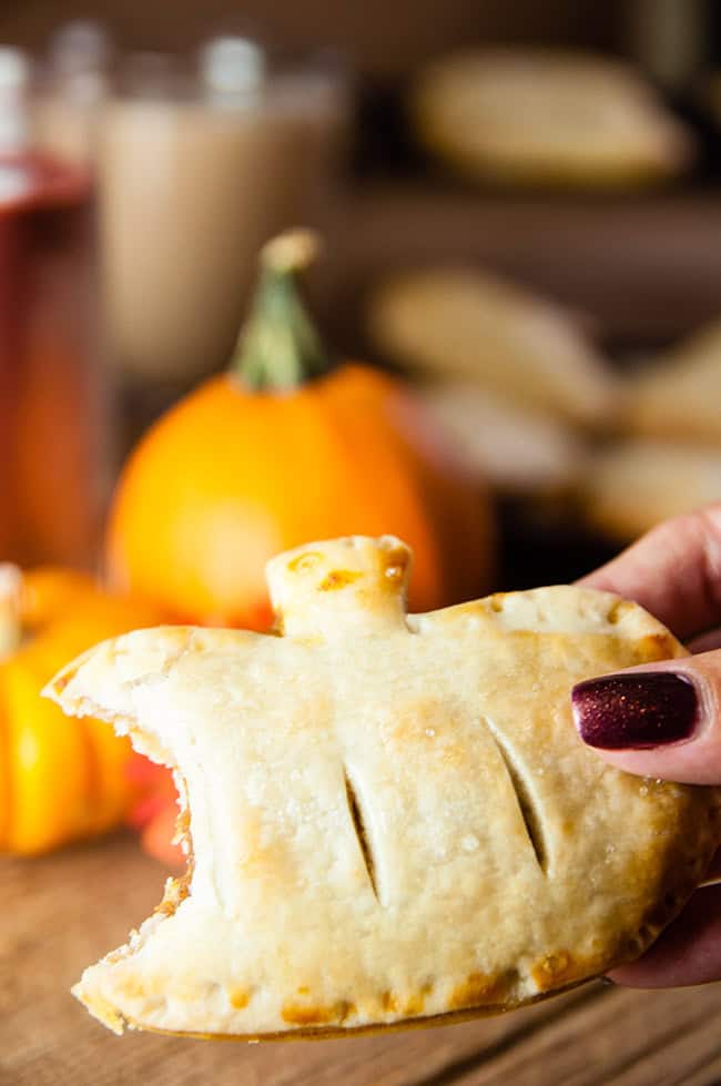 A mini pumpkin pie with a bite taken out of it in front of pumpkins and coffee.