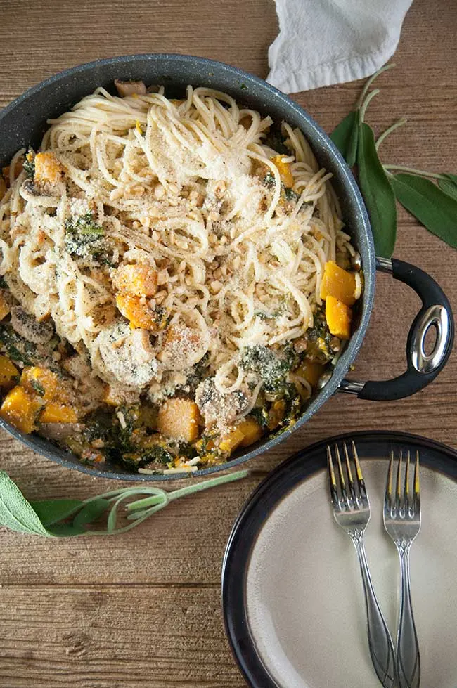 Winter Vegetable Pasta with Sauteed Butternut Squash, Kale, Mushrooms and Walnuts in a big pan with a plate and forks on wood