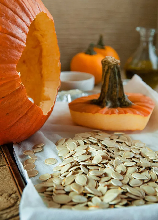 a hollowed out pumpkin on its side with the top cut off and a tray of pumpkin seeds
