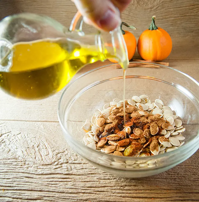 Pouring olive oil into a bowl of pumpkin seeds and spices