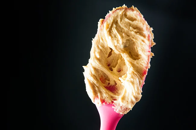 Cookie dough on a pink spoon against a black background