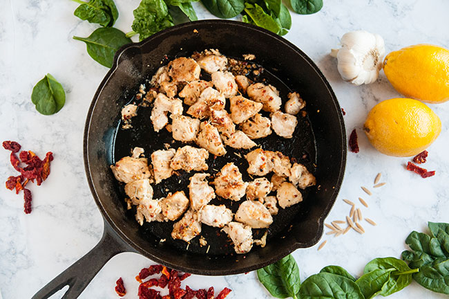 Cooked chicken breast cut into cubes in a cast iron pan on a light background