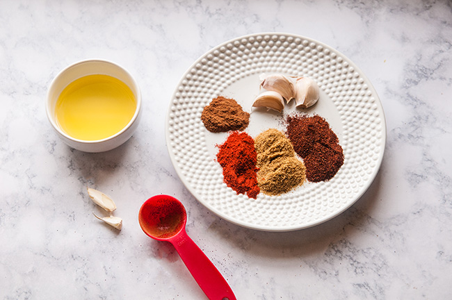 A plate of spices and garlic with a side of olive oil on a light background