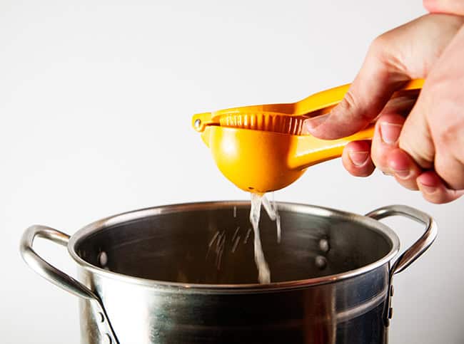 Lemon being squeezed with a citrus squeezer into a silver stock pot