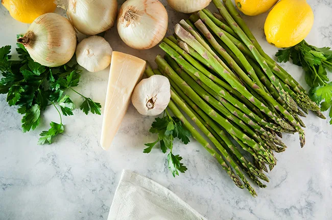 Onions, asparagus, parsley, and lemon on a white marble background