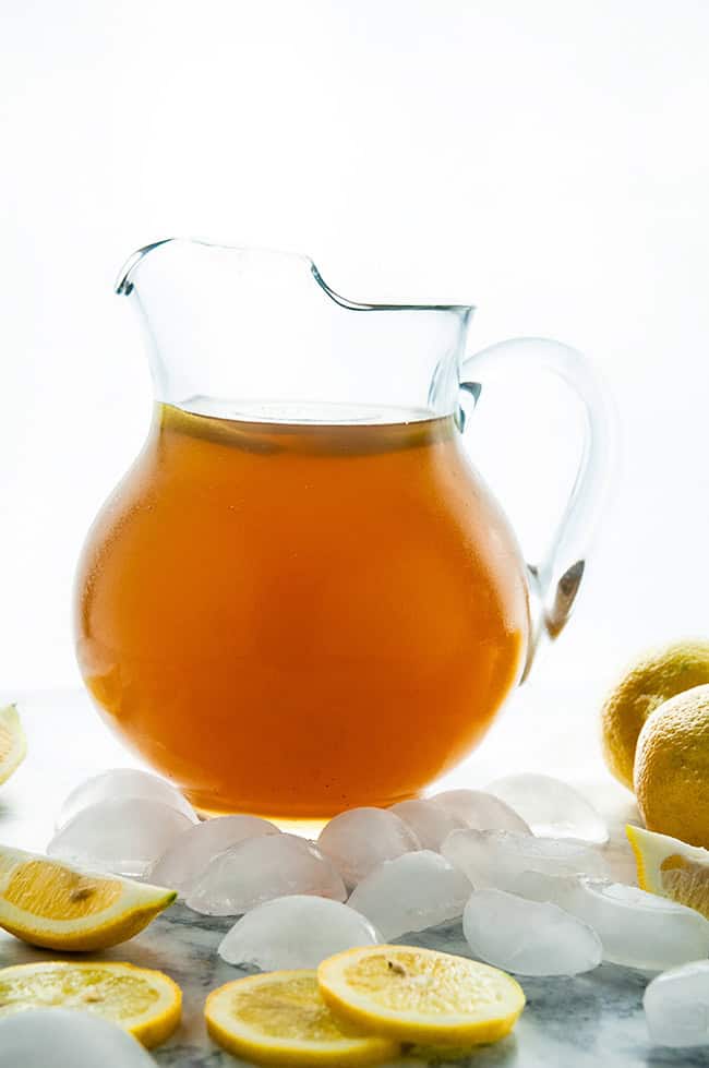 Homemade Iced Tea in a glass pitcher with lemons and ice cubes on white