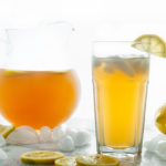 Homemade Iced Tea in a glass and glass pitcher with lemons and ice cubes on white