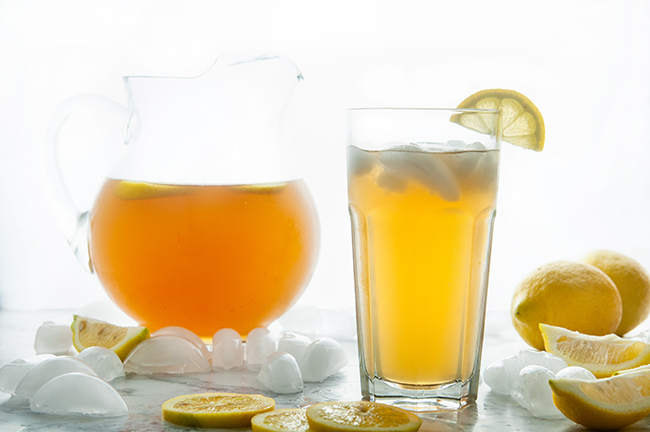 Homemade Iced Tea in a glass and glass pitcher with lemons and ice cubes on white