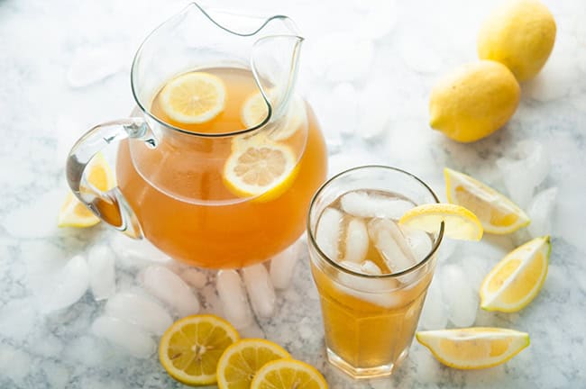 Homemade Iced Tea in a glass and glass pitcher with lemons and ice cubes on white