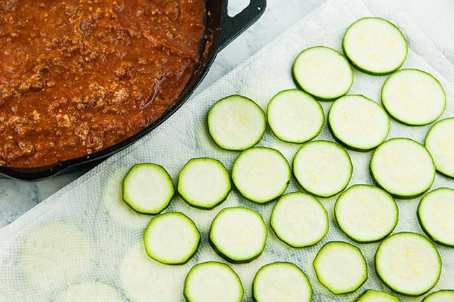 Zucchini slices next to a skillet of meat sauce