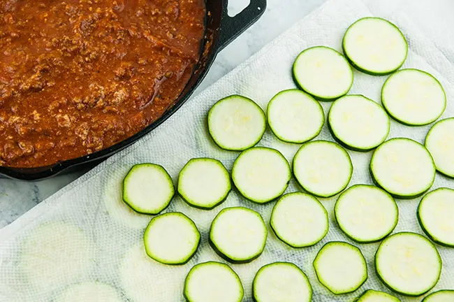 Zucchini slices next to a skillet of meat sauce