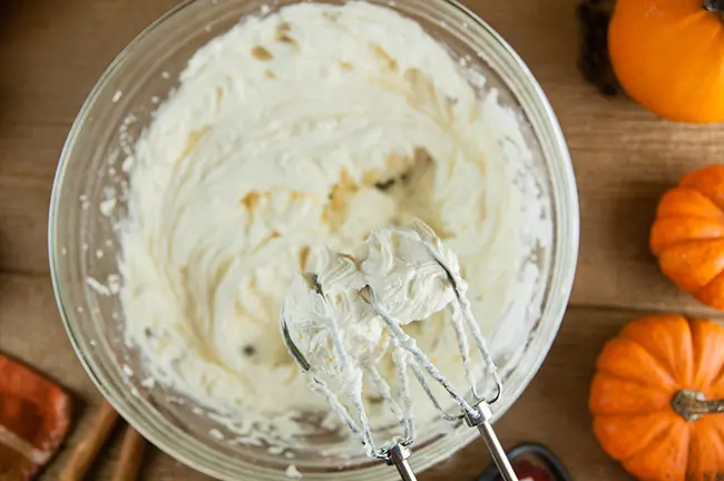 Boozy Pumpkin Spice Buttercream in a bowl on wood with pumpkins and a hand mixer