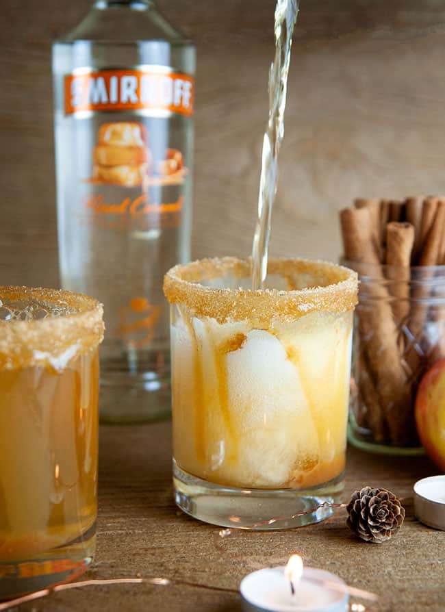 sparkling cider being poured into an Old Fashioned glass that's been rimmed with caramel and brown sugar on wood