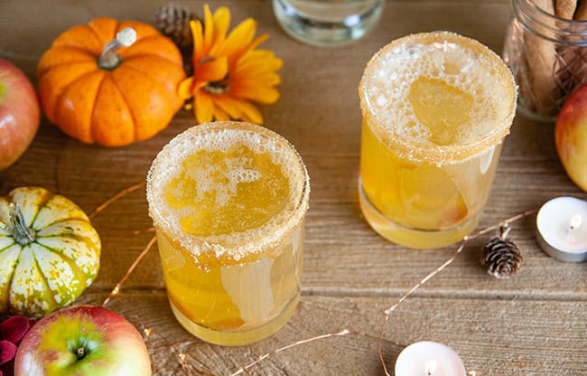 Sparkling Caramel Apple Screwdrivers on wood with pumpkins, apples, and candles