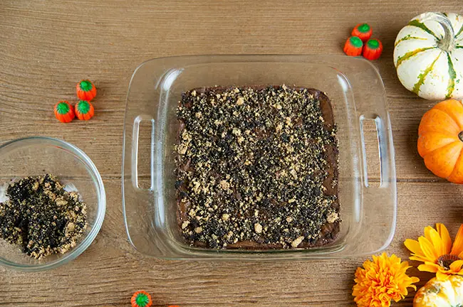 Bowl of graham cracker and oreo crumbs next to brownies covered in crumbs on wood