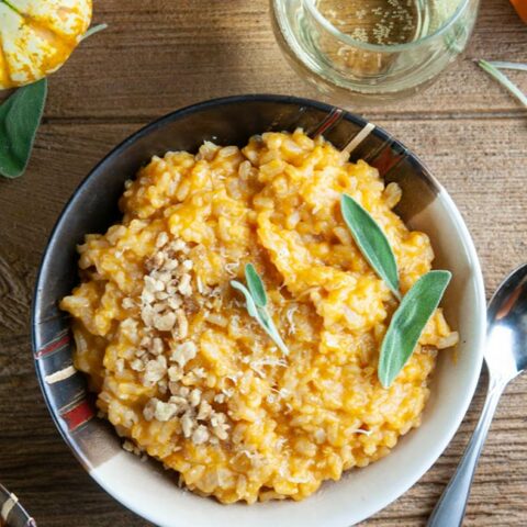 A bowl of pumpkin risotto on wood with wine and pumpkins