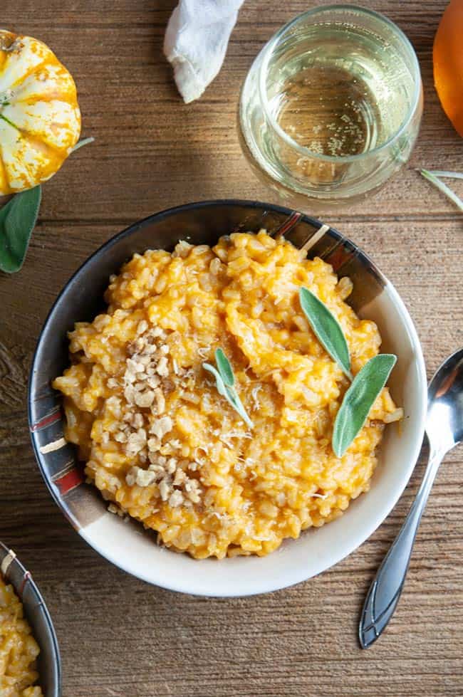 A bowl of pumpkin risotto on wood with wine and pumpkins