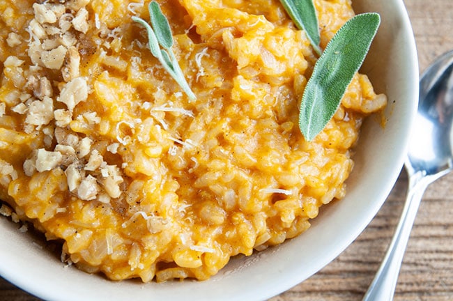 A bowl of pumpkin risotto garnished with sage, walnuts, and parmesan