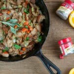 A skillet of Classic Homemade Stuffing on a wood background with orange slices, spice jars, and sage leaves