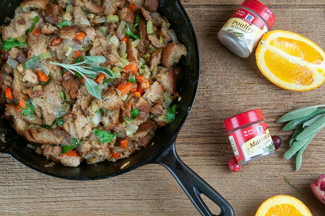 A skillet of Classic Homemade Stuffing on a wood background with orange slices, spice jars, and sage leaves