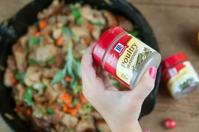 A child's hand holding McCormick® Poultry Seasoning over a pan of homemade stuffing