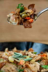 A spoonful of Classic Homemade Stuffing above a pan of stuffing on wood background