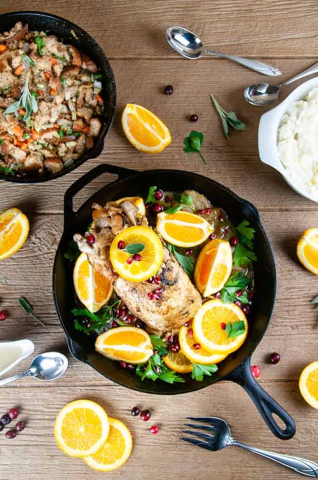 Garlic Roasted Turkey breast in a cast iron skillet on wood with mashed potatoes, stuffing, and orange slices