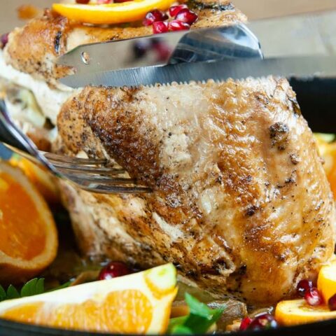 A knife cutting into a roast turkey breast on wood background