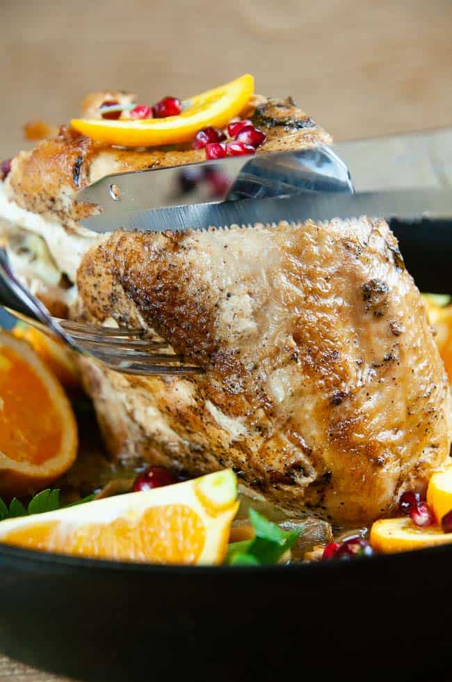 A knife cutting into a roast turkey breast on wood background