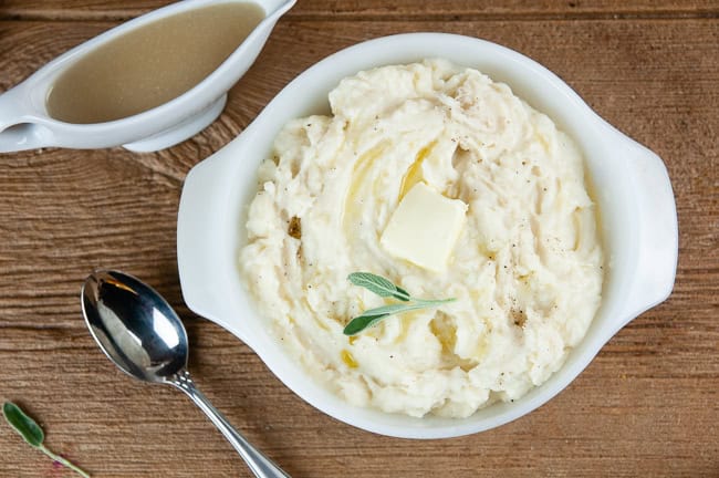 Instant Pot Mashed Potatoes in a white porcelain dish on wood with a gravy boat and spoon