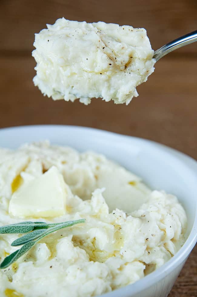 A big scoop of Instant Pot mashed potatoes on a wood background above a bowl of mashed potatoes