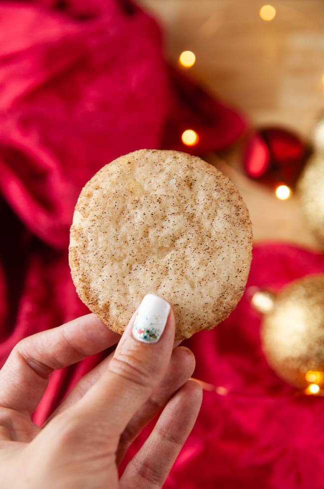Hand holding a snickerdoodle in front of a red cloth and holiday ornaments store bought sugar cookie dough hacks