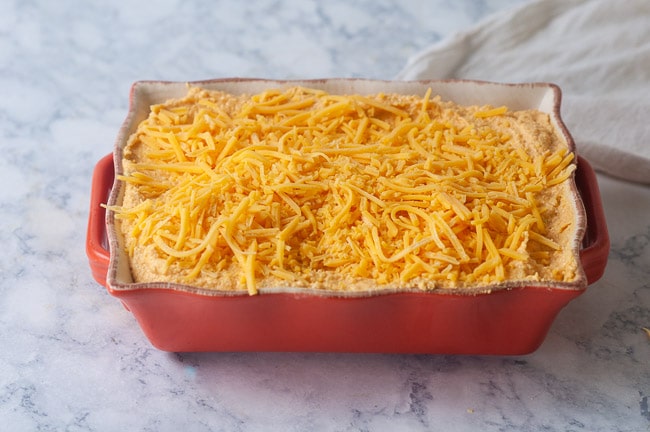 Dip covered in cheese in an orange casserole dish on white