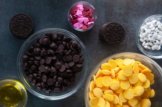 Ingredients for bumblebee cookies: yellow candy melts, chocolate chip, candy eyes, oil, Oreos, heart sprinkles