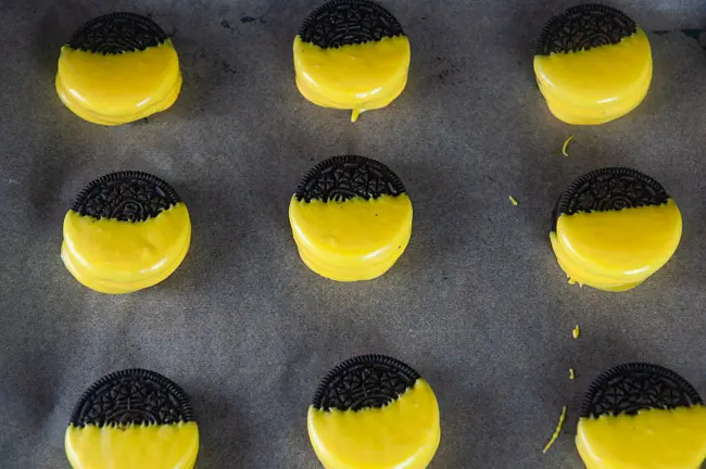 Oreos dipped 2/3s of the way into yellow melted candy on a tray lined with parchment