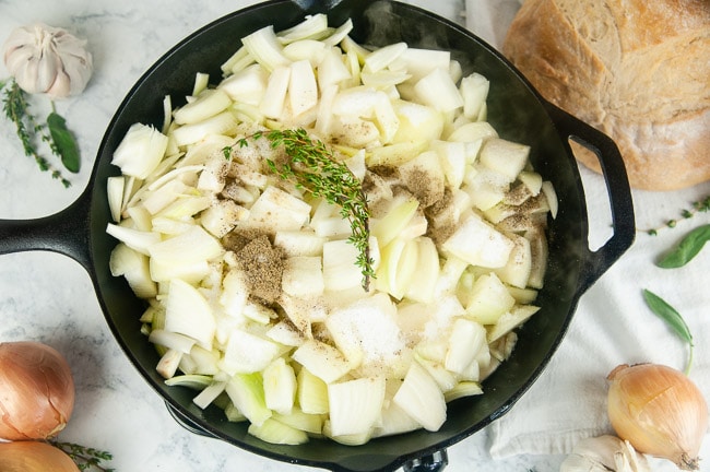 A large skillet full of sliced onions and herbs