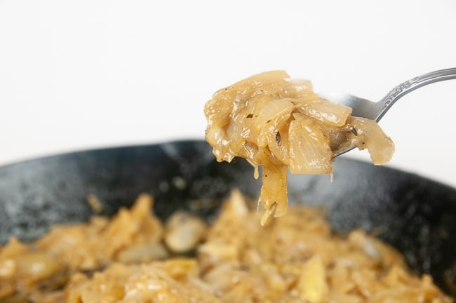 A spoonful of caramelized onions over a cast iron skillet full of caramelized onions on white
