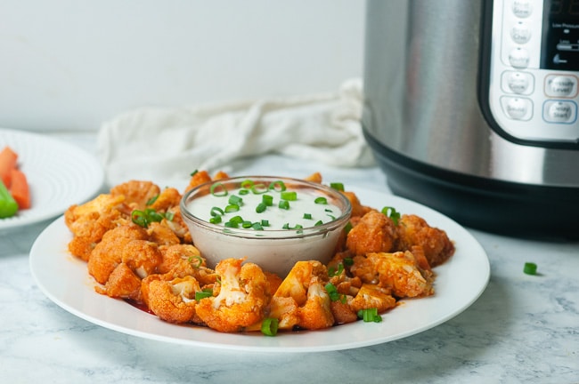 Instant Pot Buffalo Cauliflower on a plate with dressing in front of an Instant Pot on white marble