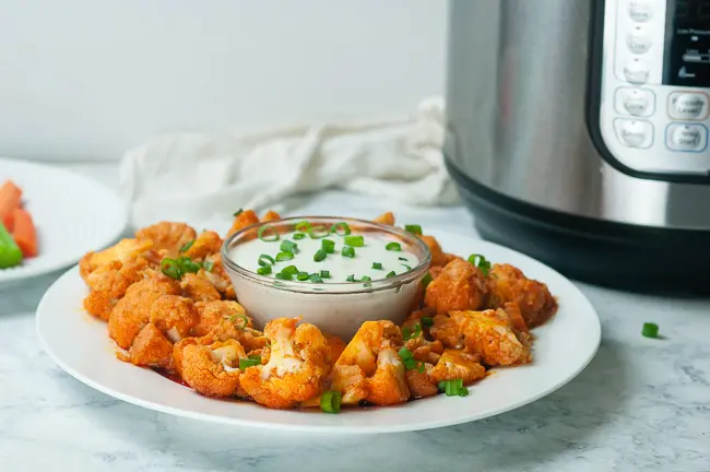 Instant Pot Buffalo Cauliflower on a plate with dressing in front of an Instant Pot on white marble