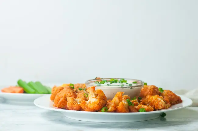 Instant Pot Buffalo Cauliflower on a plate sitting on white marble with a plate of carrots and celery in the background
