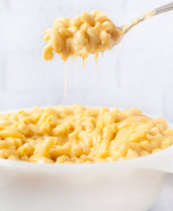 A spoon full of Instant Pot mac and cheese being lifted out of a white dish in a white kitchen