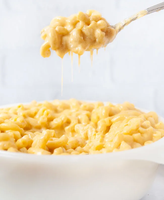 A spoon full of Instant Pot mac and cheese being lifted out of a white dish in a white kitchen