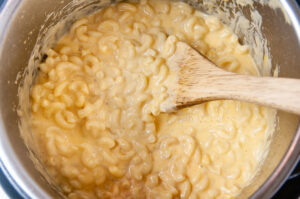 Macaroni and cheese in the inner liner of an Instant Pot with a wood spoon