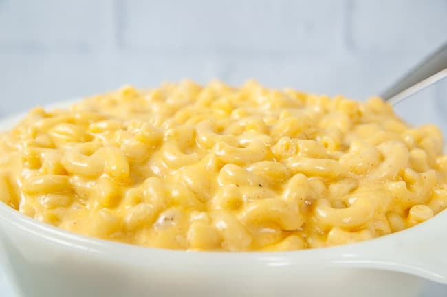 A spoon full of Instant Pot mac and cheese being lifted out of a white dish in a white kitchen